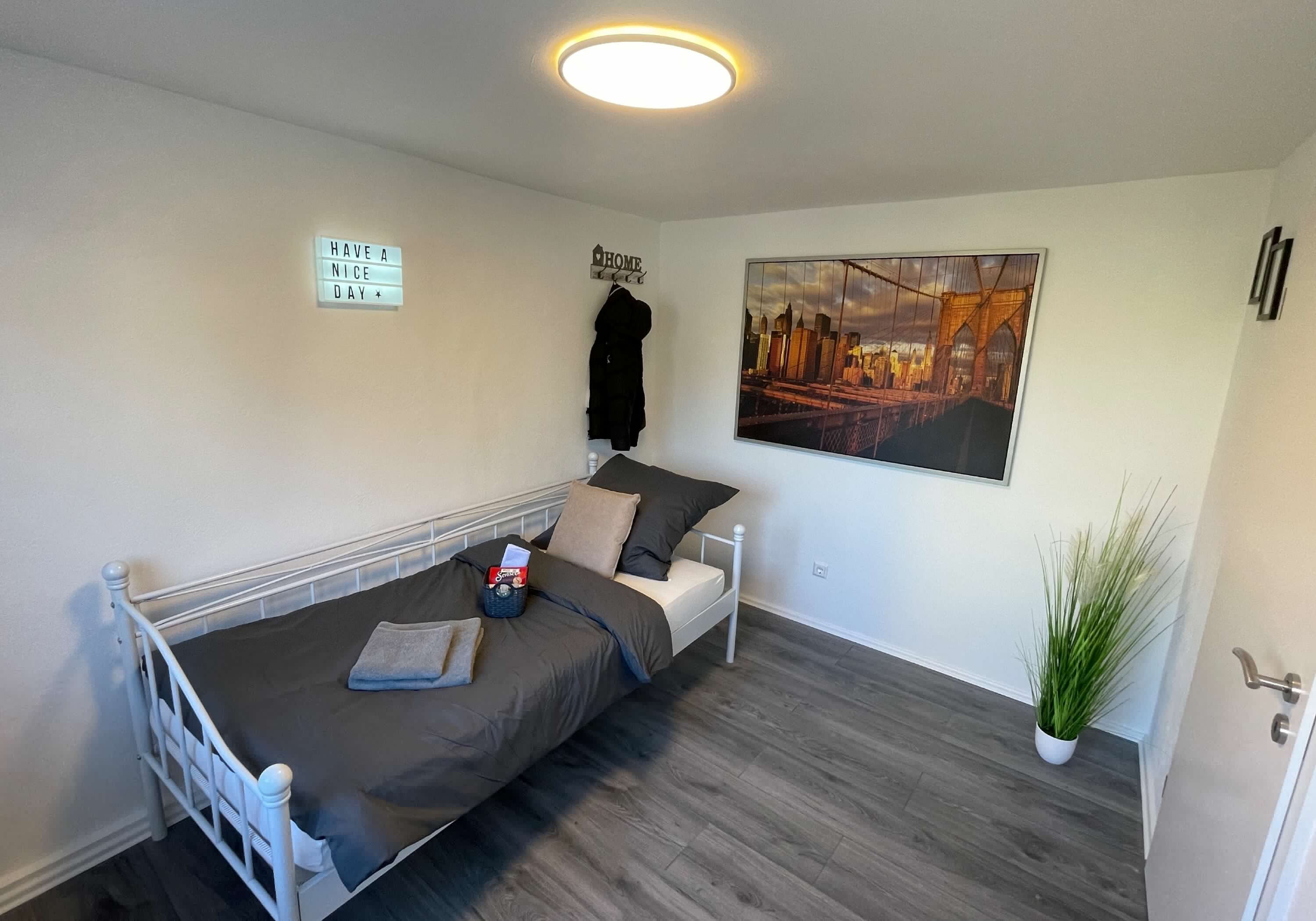 Schlafzimmer mit bezogenem Bett, Garderobe und Wandbild